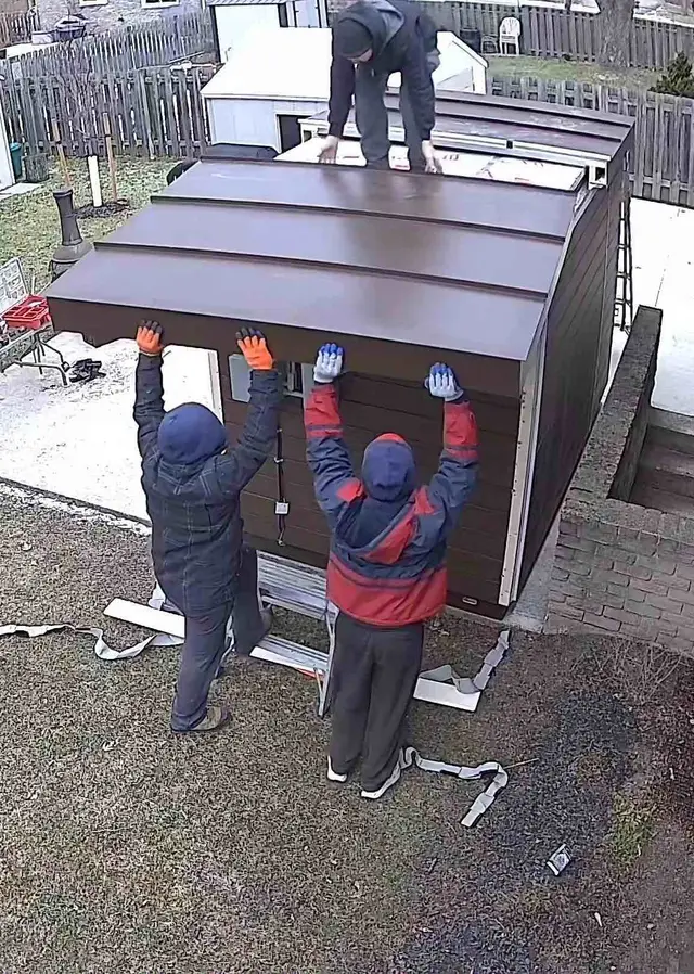Two installers lifting one half of a two-piece roof onto a sauna