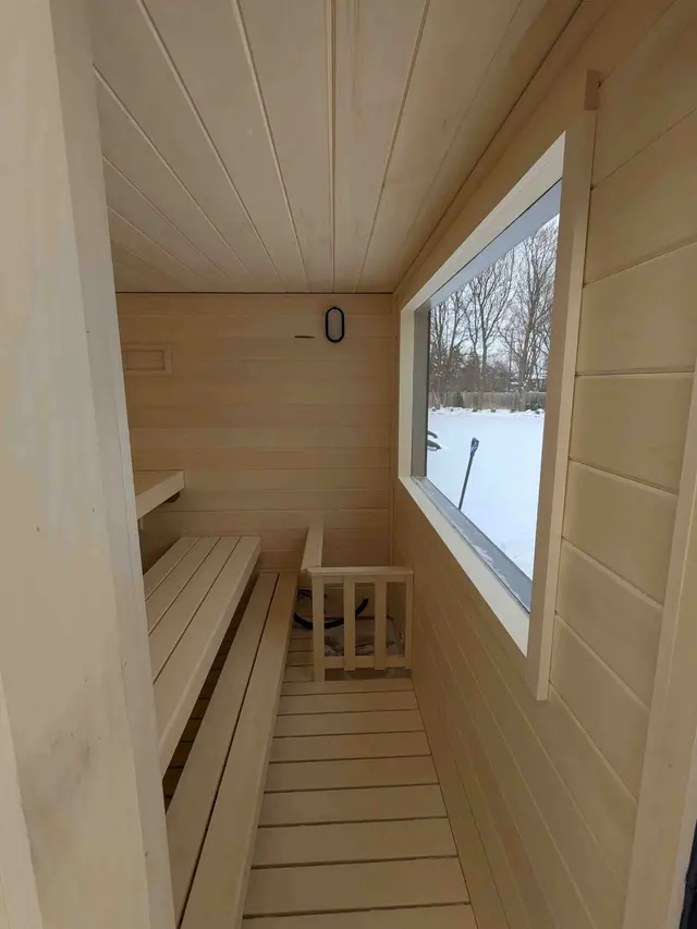 Interior of a 92" x 76" sauna with benches and a large front window looking onto snow