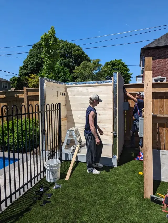 Installer assembling a sauna beside a pool, with three walls up