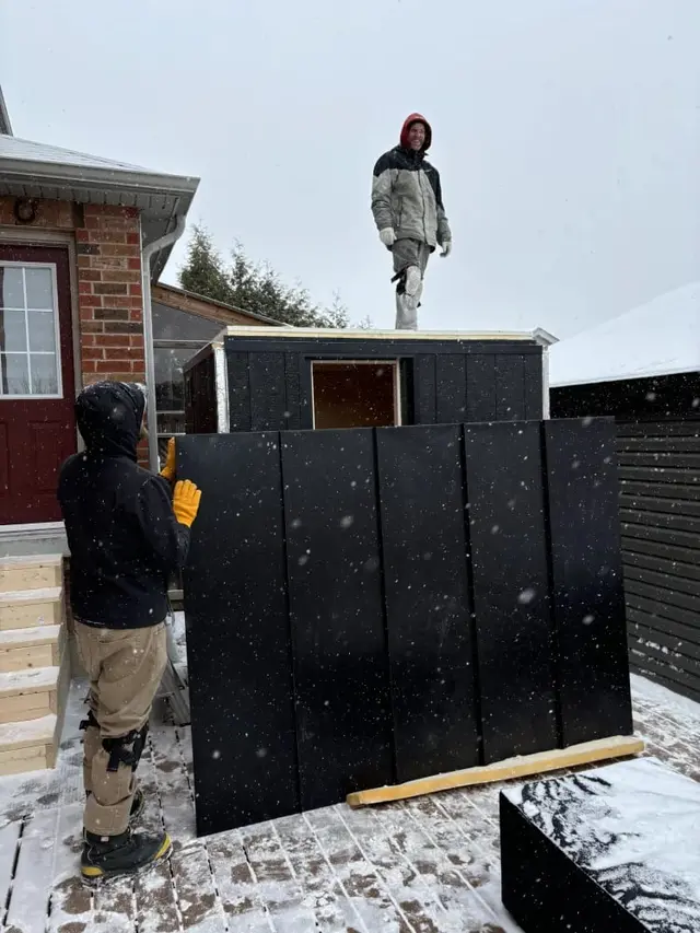 Installers assembling a black sauna in the snow