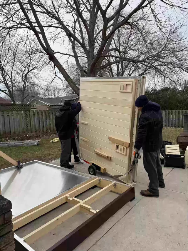 Installers setting a wall panel onto a sauna base
