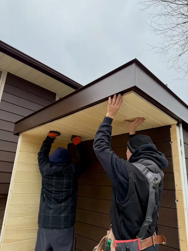 Two installers fitting the porch roof of a brown sauna