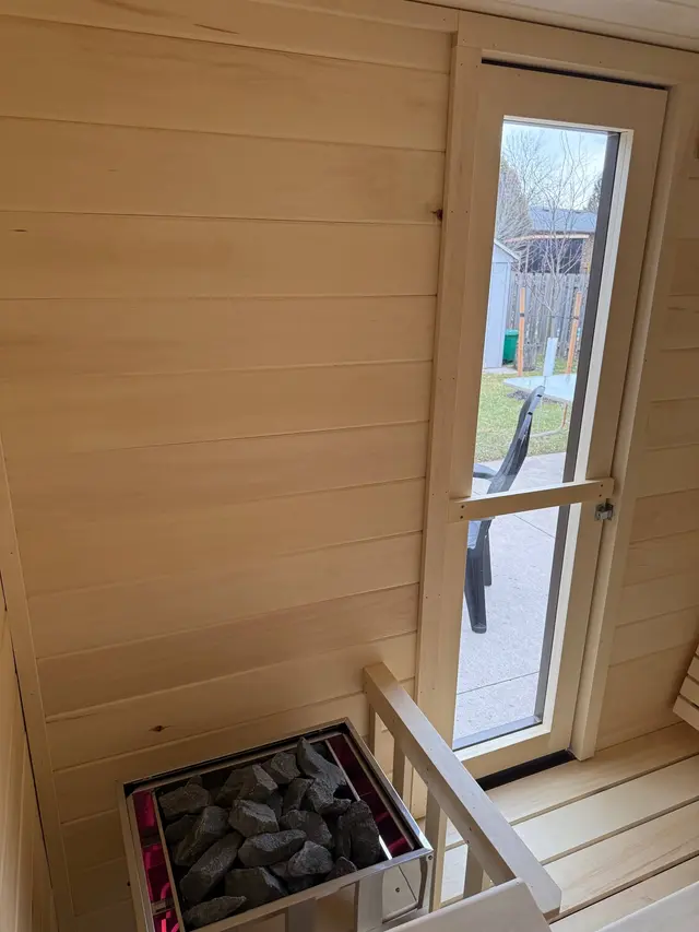Heater and railing inside an aspen sauna, beside the glass door