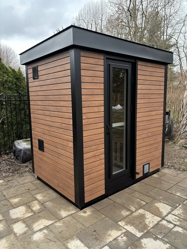 Woodgrain sauna with black trim on a paver patio