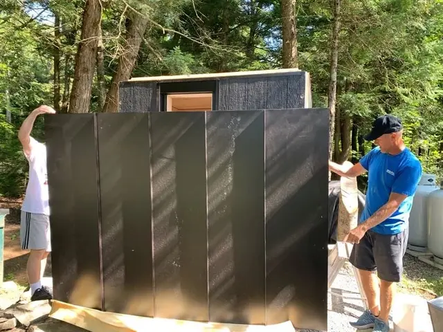 Two installers lifting a black wall panel into place