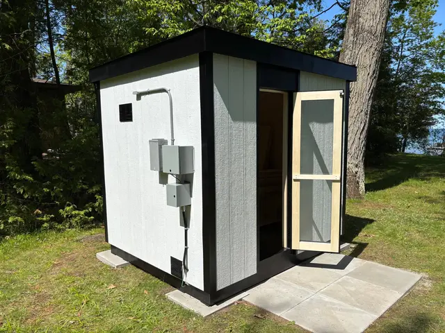 White sauna with the door open and an electrical box, on a paver pad