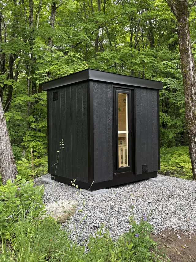 Black sauna on a gravel pad in a wooded yard
