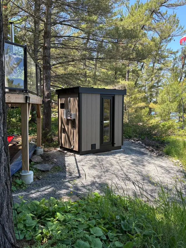 Grey sauna on a gravel pad in a wooded yard