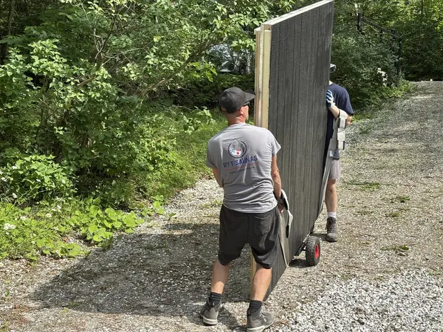 Two installers moving a black wall panel along a gravel path