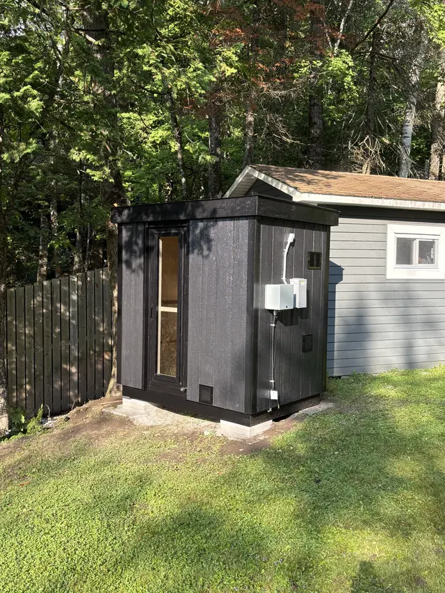 Black sauna with an electrical box in a grassy yard