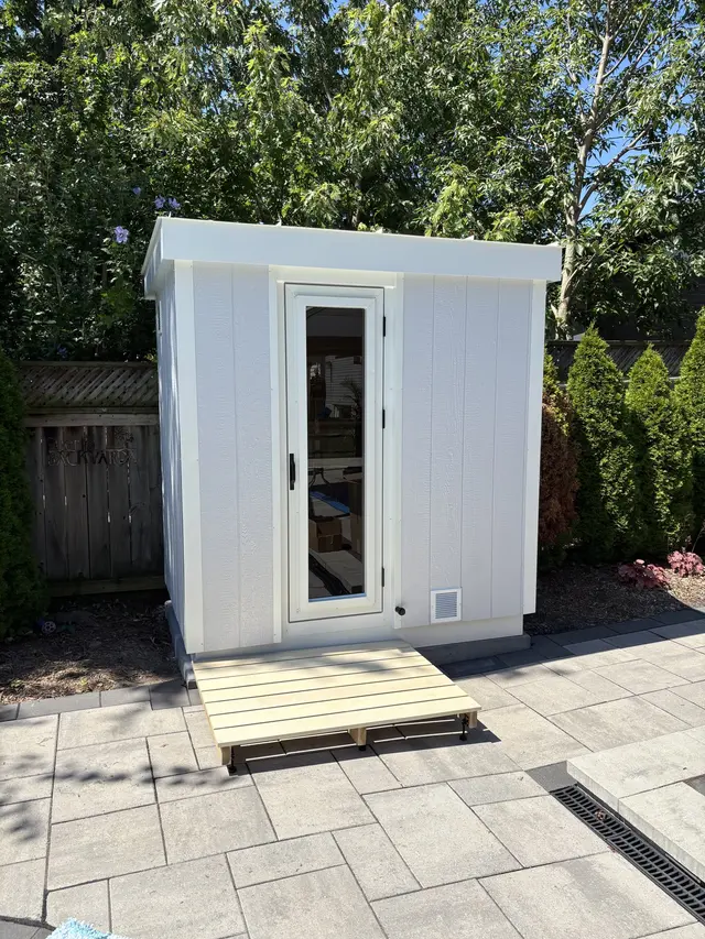 White sauna with a glass door on a paver patio