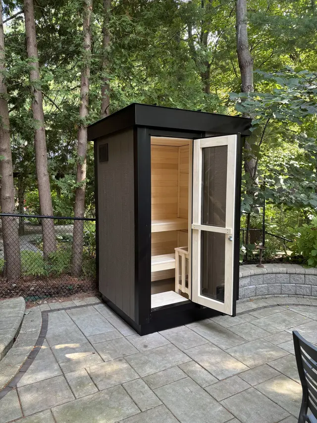 Black sauna with the door open on a paver patio