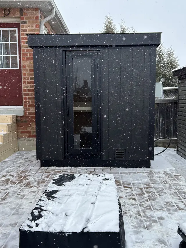 Black sauna on a patio in falling snow