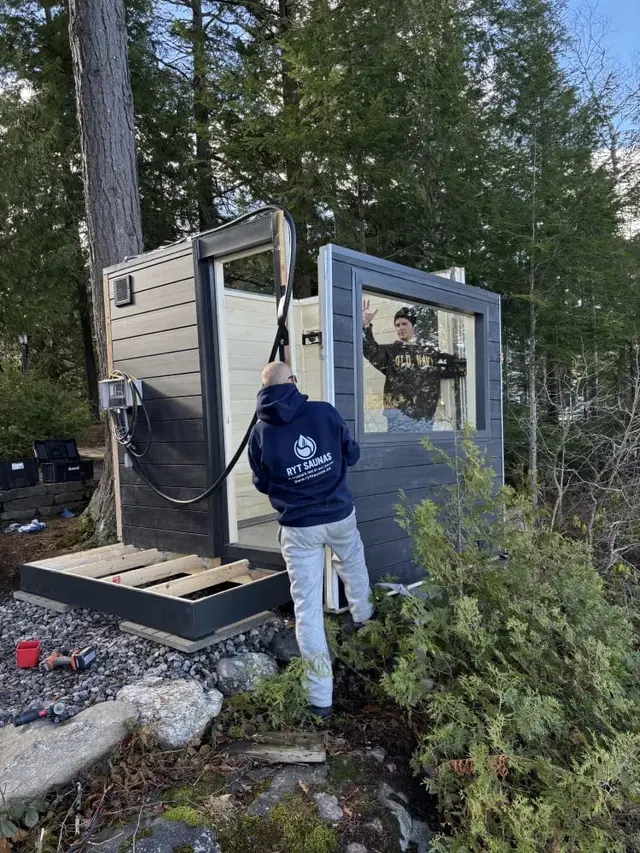 Installers assembling a grey sauna in a wooded yard