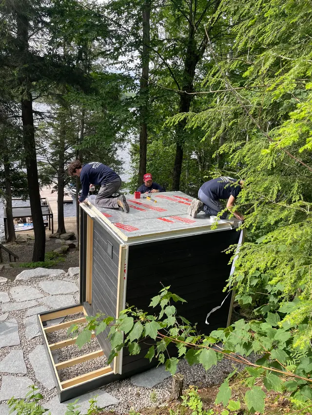 Installers assembling a sauna on a wooded hillside