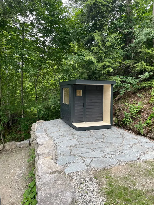 Black sauna on a flagstone patio beside a rock wall