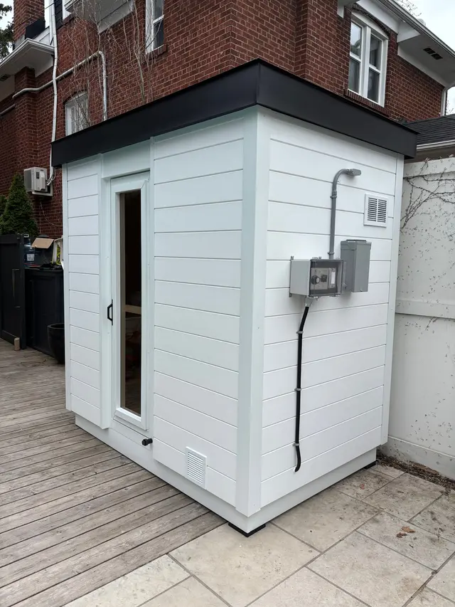 White sauna with an electrical box on a deck beside a house