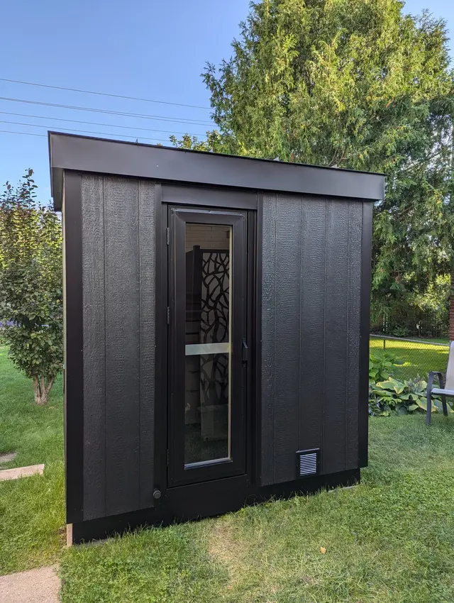 Black sauna with a decorative glass door on a lawn