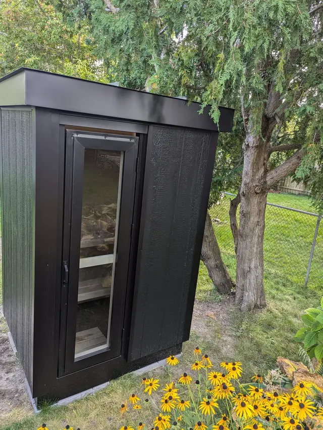 Black sauna with a glass door beside yellow flowers