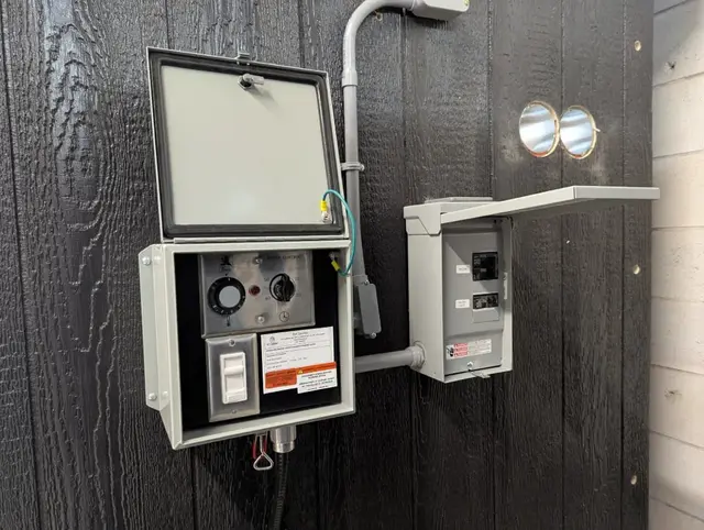 Sub-panel and control box mounted on a black sauna wall