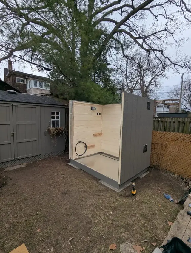 Grey sauna being assembled next to a shed