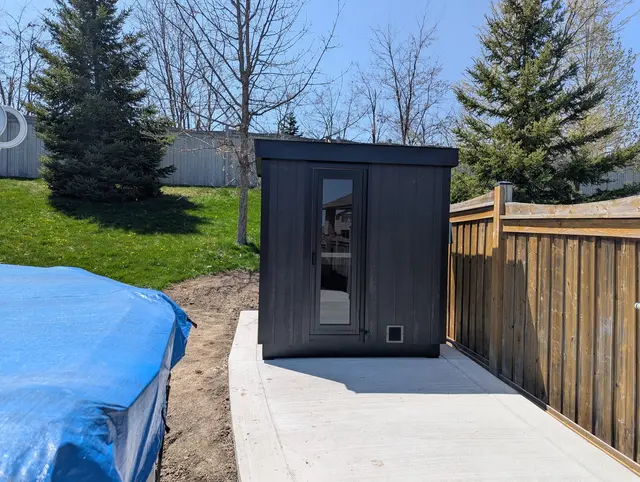 Black sauna on a concrete pad beside a fence