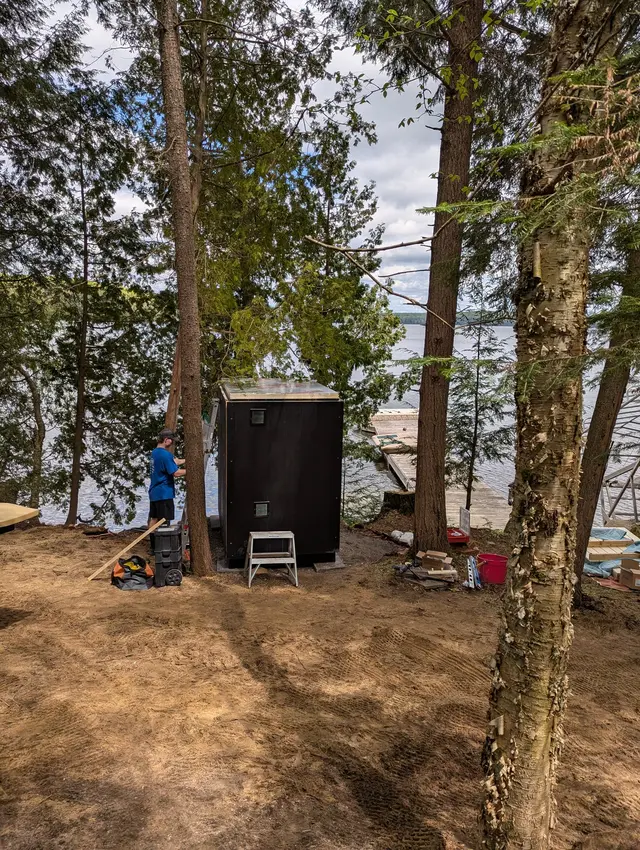 Installers setting up a sauna on a wooded lakeside lot
