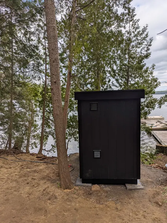 Black sauna on a sand pad among trees by a lake