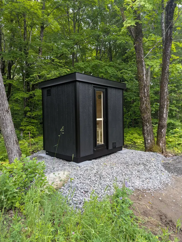 Black sauna on a gravel pad among trees