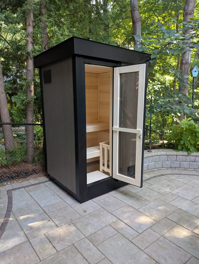 Black sauna with the glass door open to the aspen interior, on a stone patio