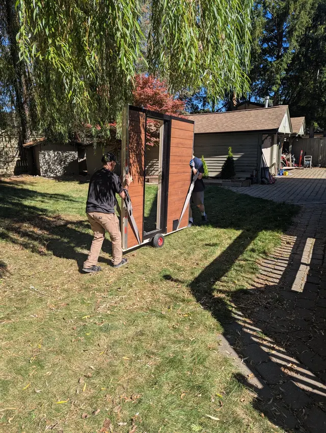 Installer moving a sauna wall panel across a lawn on a dolly