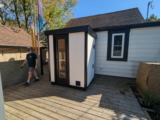 White and black sauna on a backyard deck, with a person walking past