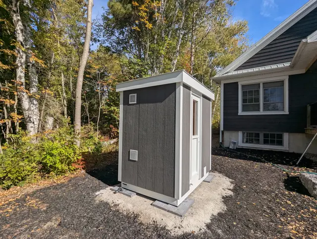 Grey sauna with white trim in a backyard garden bed