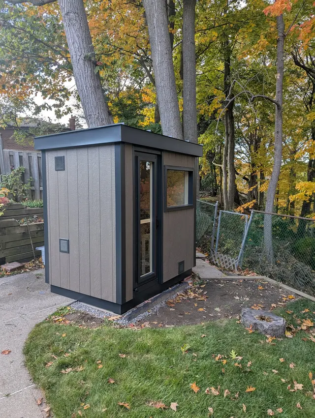Grey sauna with a side window on a lawn in autumn