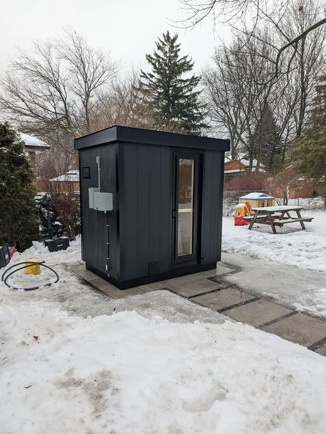 Black sauna with an electrical box on a snowy patio