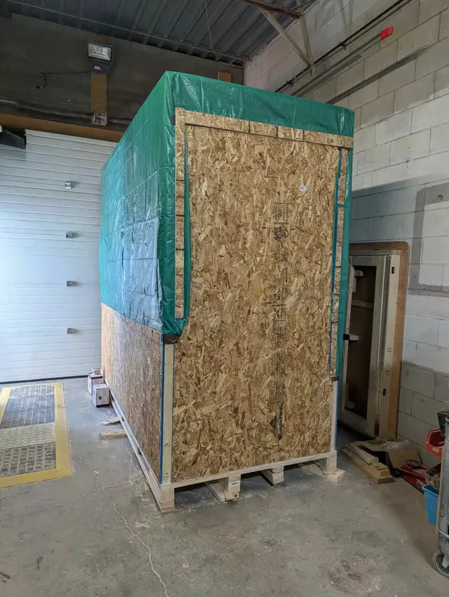 Sauna wrapped in plywood and a tarp in the shop, ready to ship