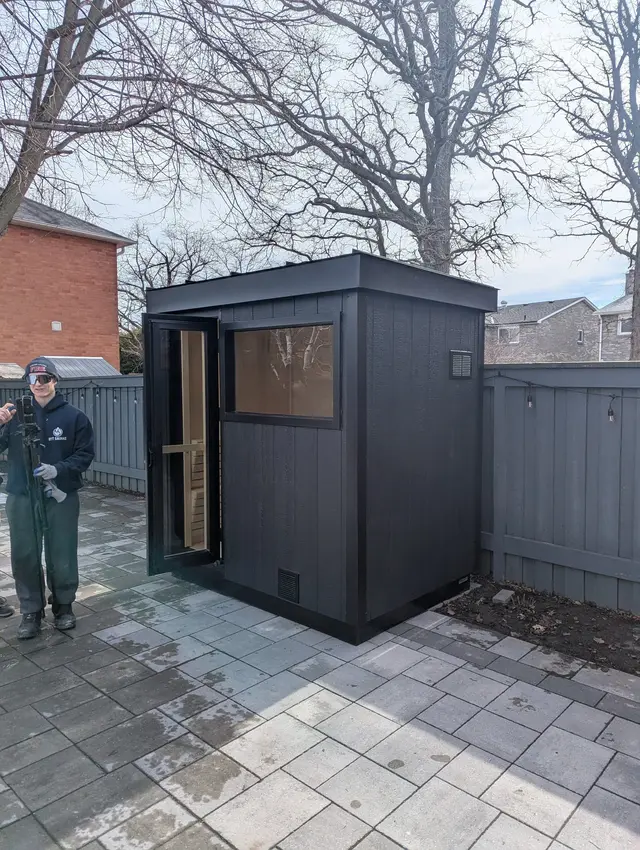 Black sauna with a front window on a paver patio, with an installer