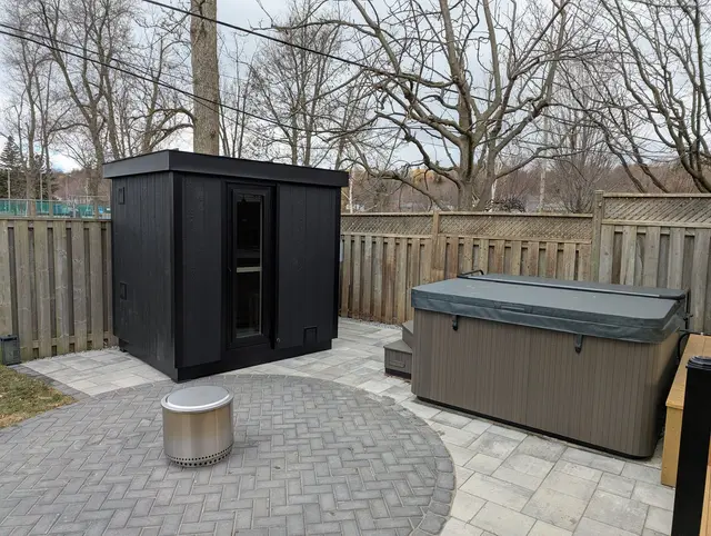 Black sauna beside a hot tub on a paver patio