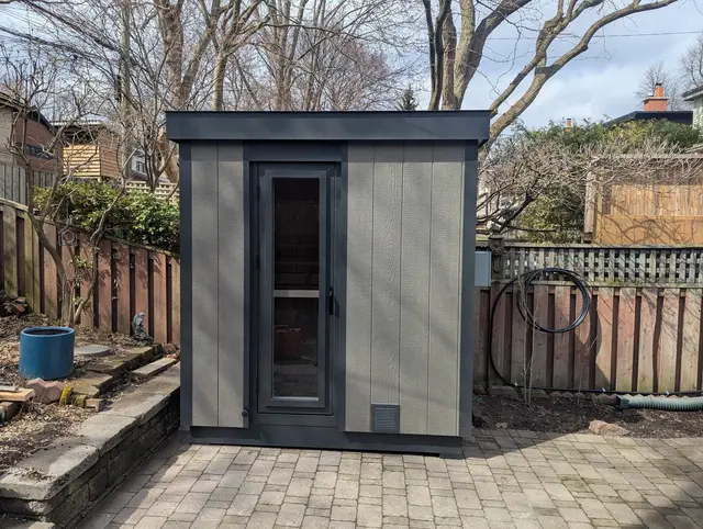 Grey sauna with a glass door on a paver patio