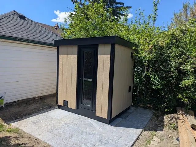 Tan and black sauna on a paver patio beside a garage
