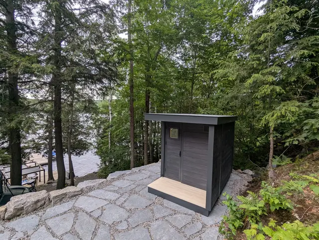 Grey sauna with a light wood porch on a stone terrace in the woods