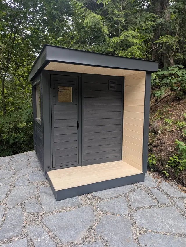 Black sauna with a light wood porch overhang on a flagstone patio