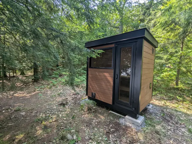 Sauna with woodgrain and black cladding in a wooded yard