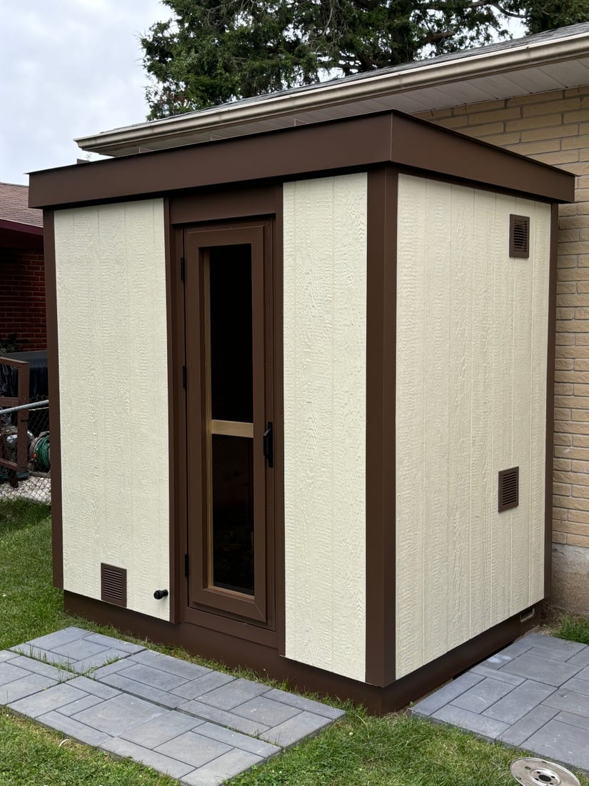 A finished Ryt Sauna with light walnut Chamclad siding and an aluminum-trimmed glass door