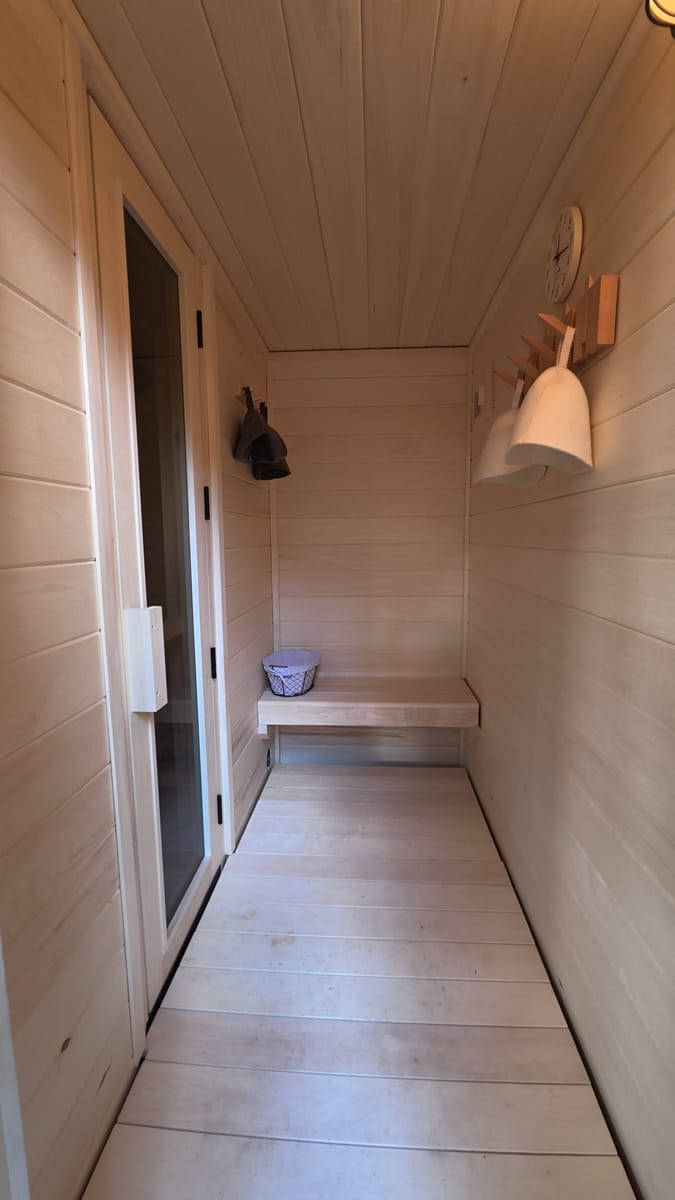 The aspen-lined interior of a Ryt Sauna change room, with a bench, a peg rail of sauna hats, and the glass sauna door on the left